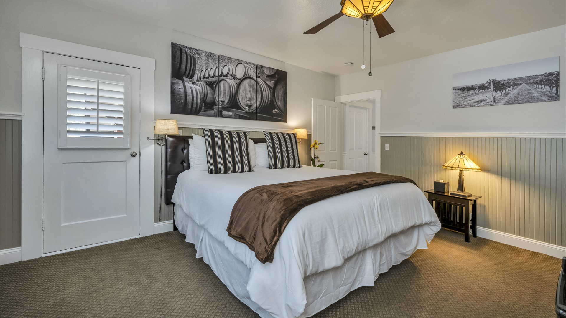 Bedroom with white walls, light gray wainscotting, light colored carpeting, white bedding, and dark wooden nightstands