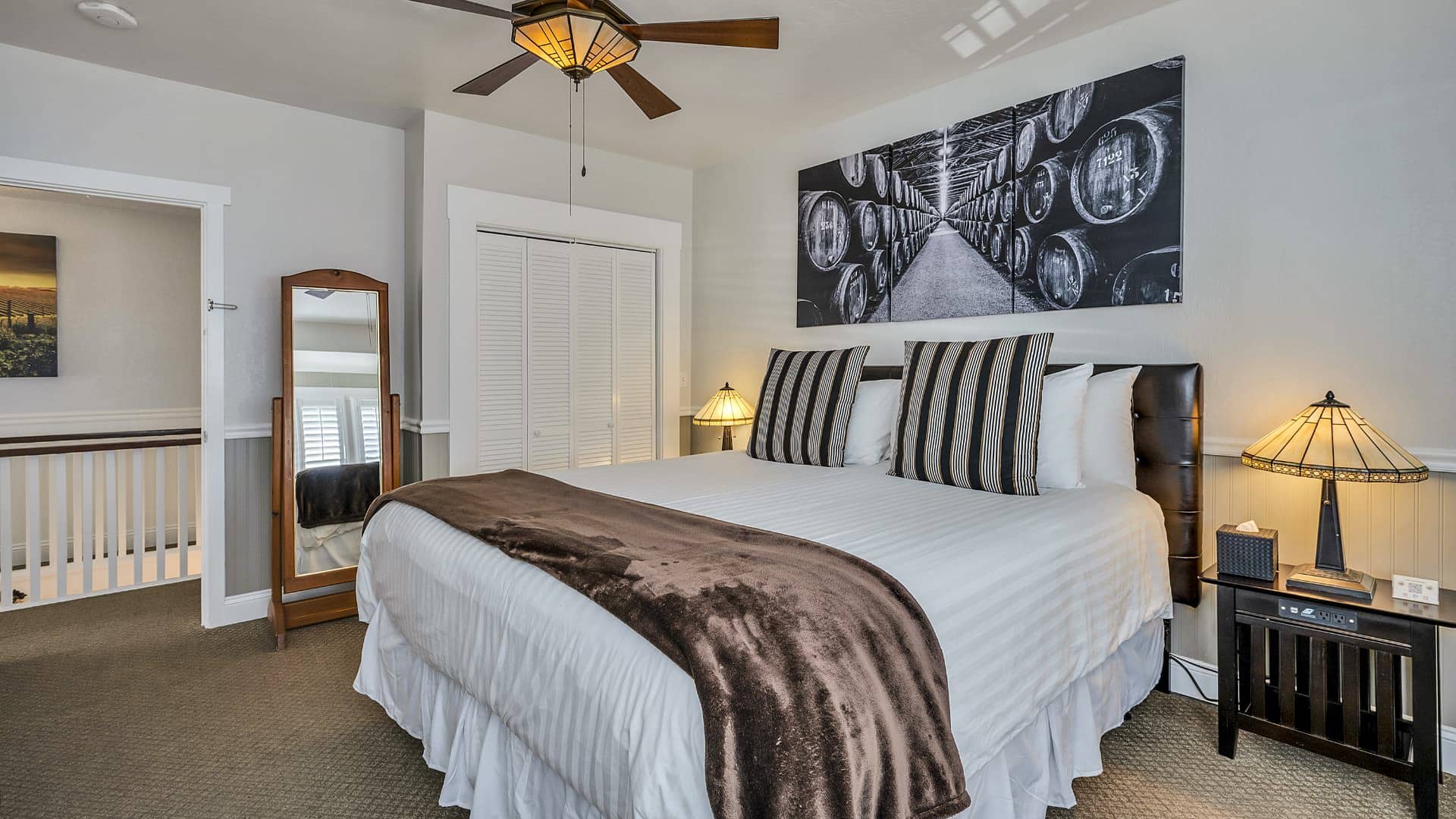 Bedroom with white walls, light gray wainscotting, light colored carpeting, white bedding, and dark wooden nightstands