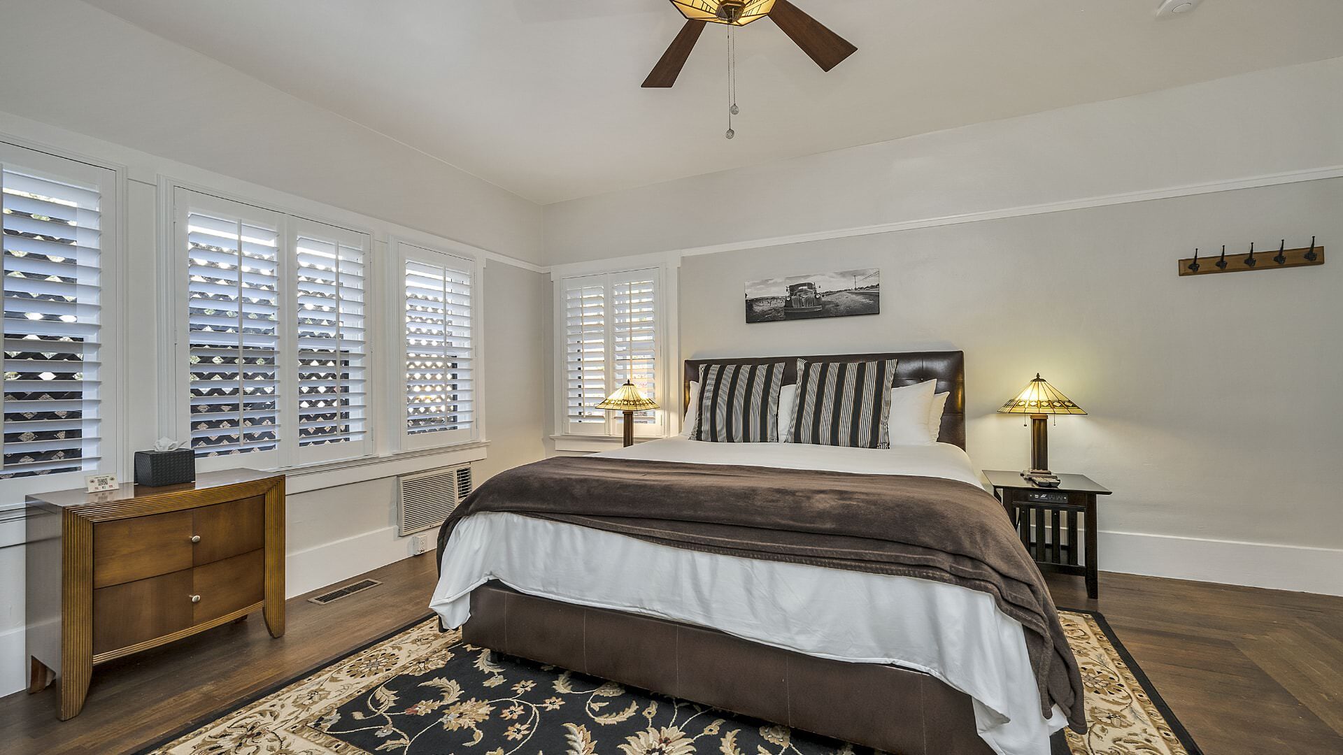 Bedroom with white walls, hardwood flooring, white bedding, and dark wooden nightstands