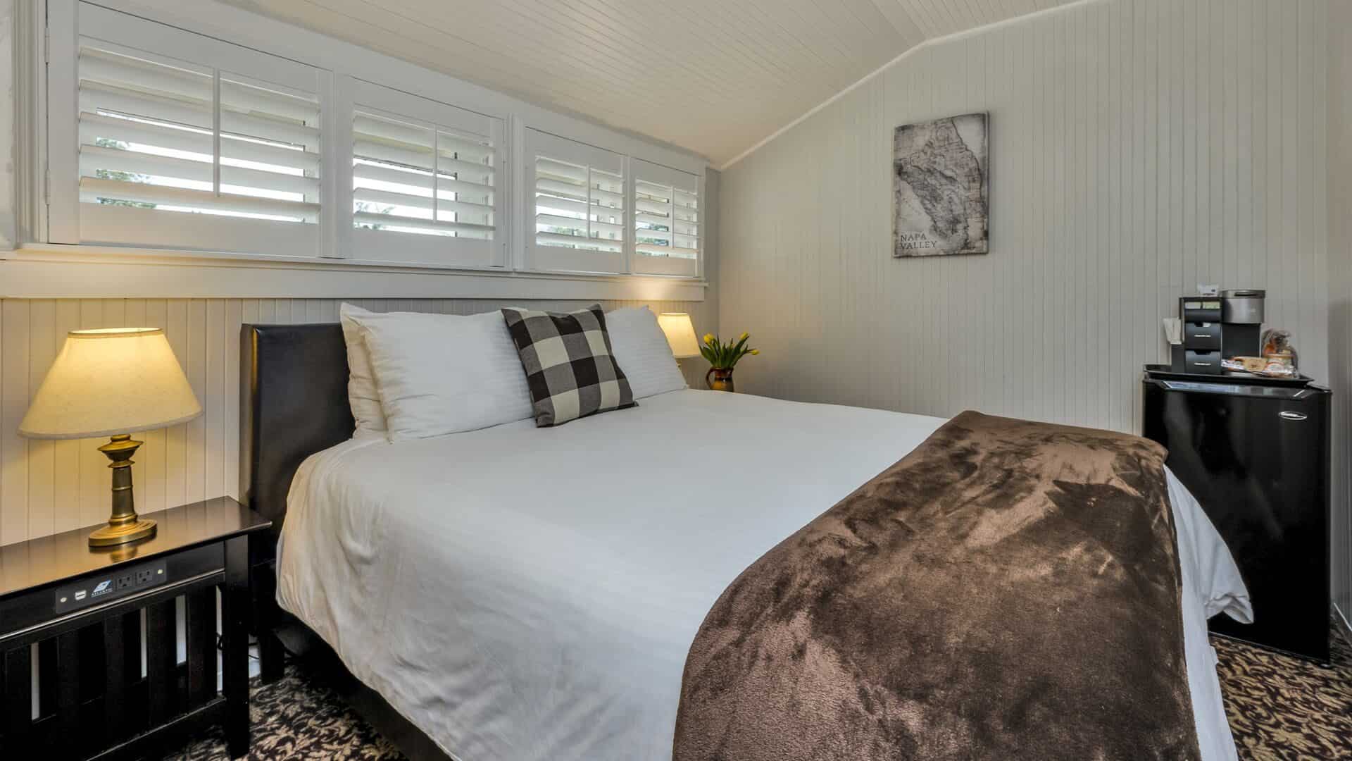 Bedroom with light gray walls, floral carpeting, white bedding, and black mini fridge