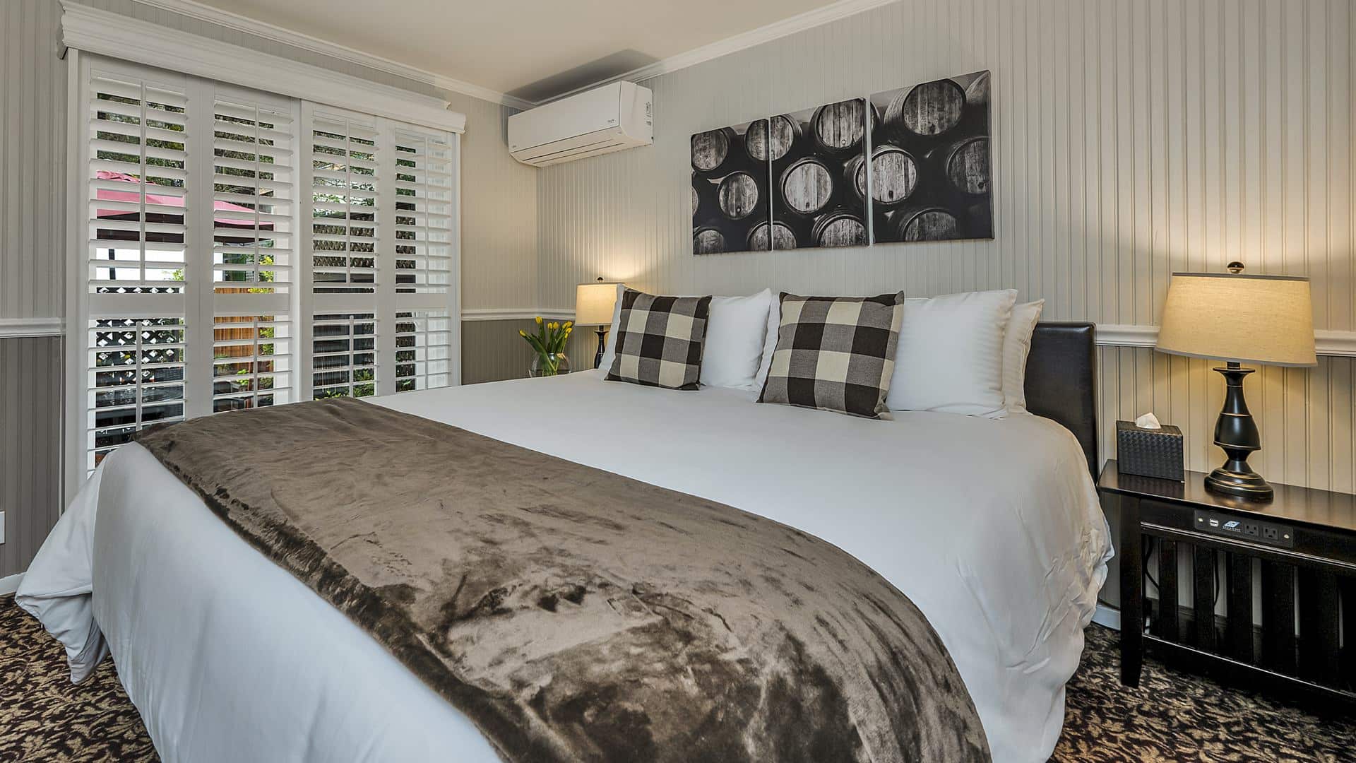 Bedroom with white walls, light gray wainscotting, floral carpeting, white bedding, and dark wooden nightstands