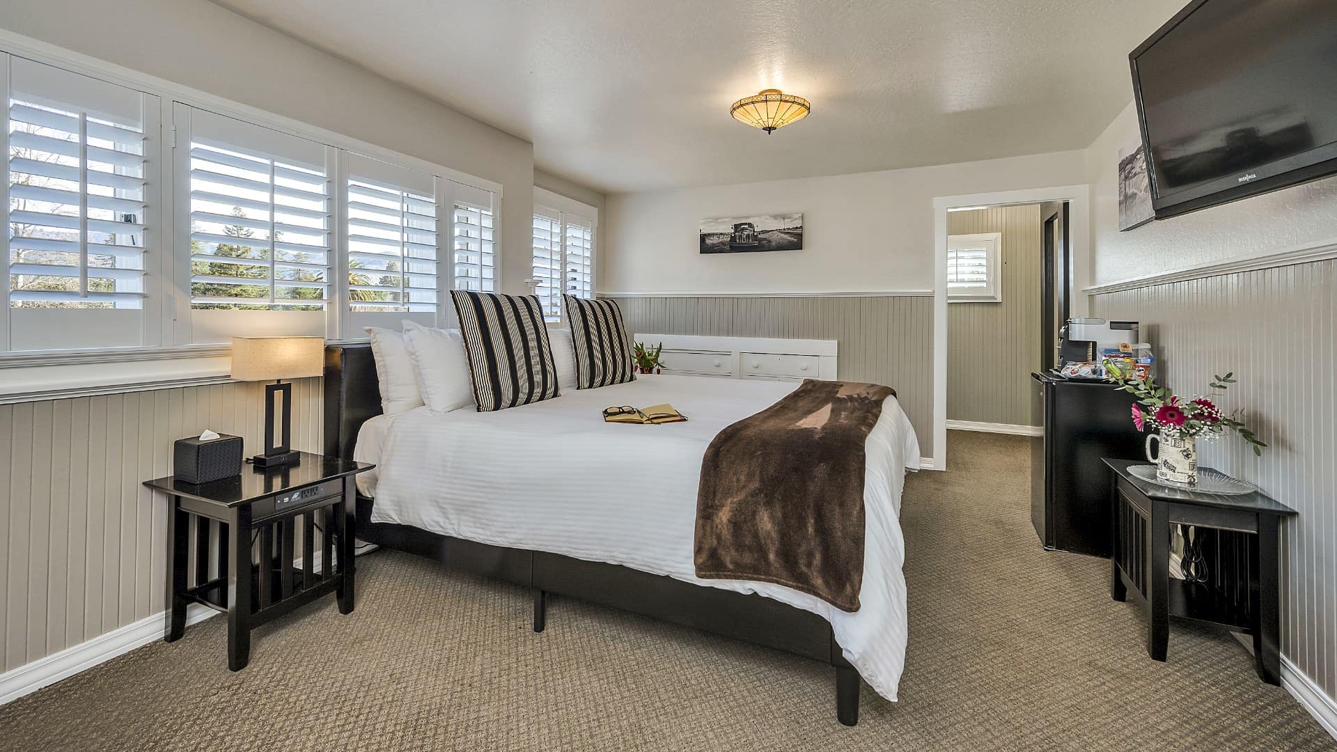 Bedroom with white walls, light gray wainscotting, light colored carpeting, white bedding, and dark wooden nightstands