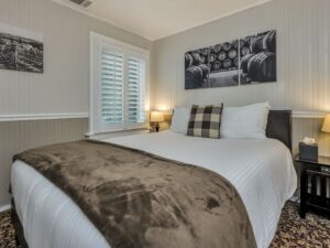 Bedroom with white walls, light gray wainscotting, floral carpeting, white bedding, and dark wooden nightstands