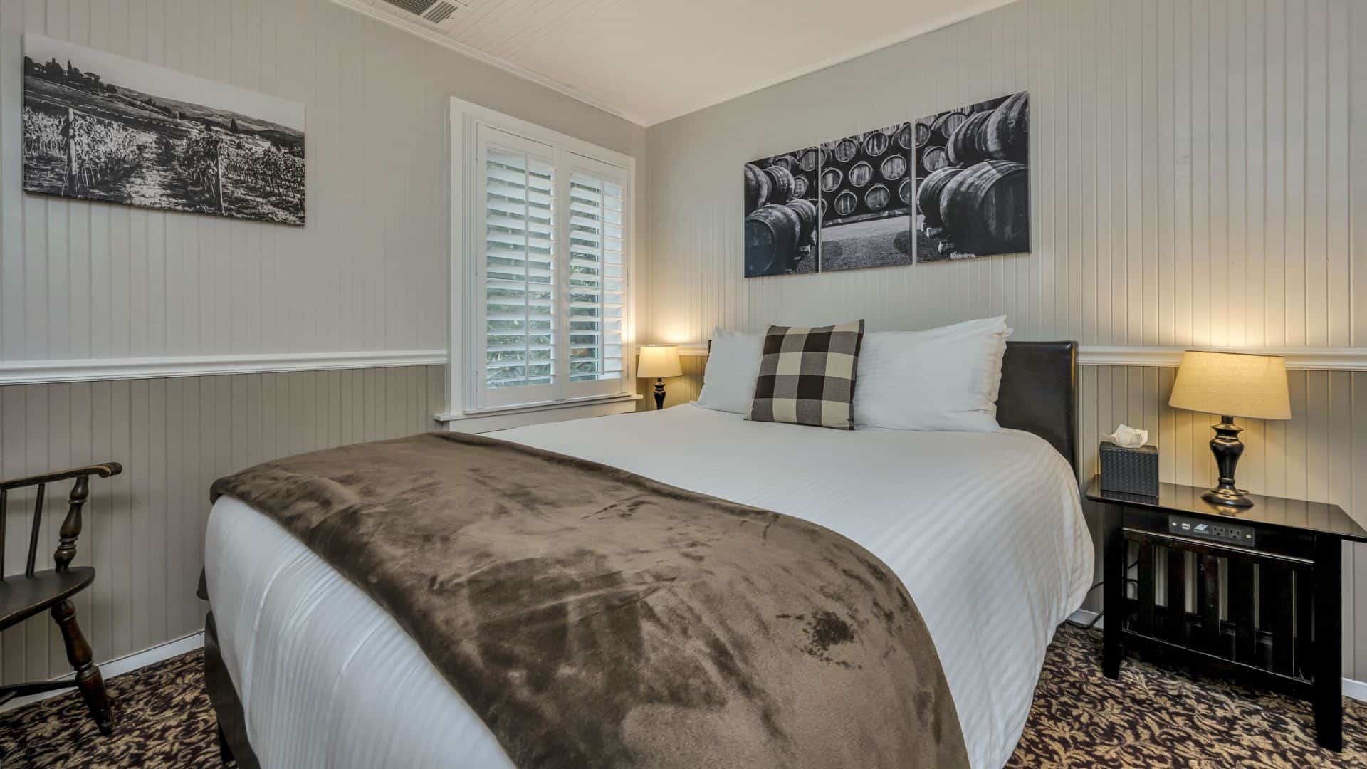 Bedroom with white walls, light gray wainscotting, floral carpeting, white bedding, and dark wooden nightstands