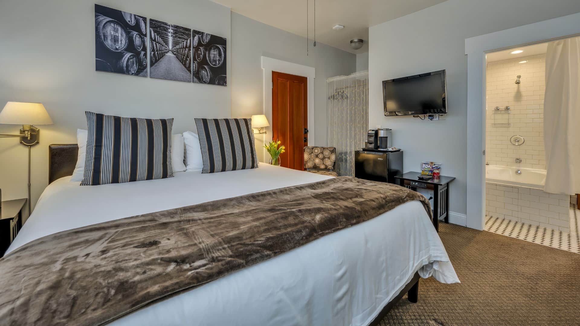 Bedroom with white walls, light colored carpeting, white bedding, black mini fridge, and dark wooden nightstands