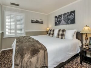 Bedroom with white walls, light gray wainscotting, floral carpeting, white bedding, and dark wooden nightstands