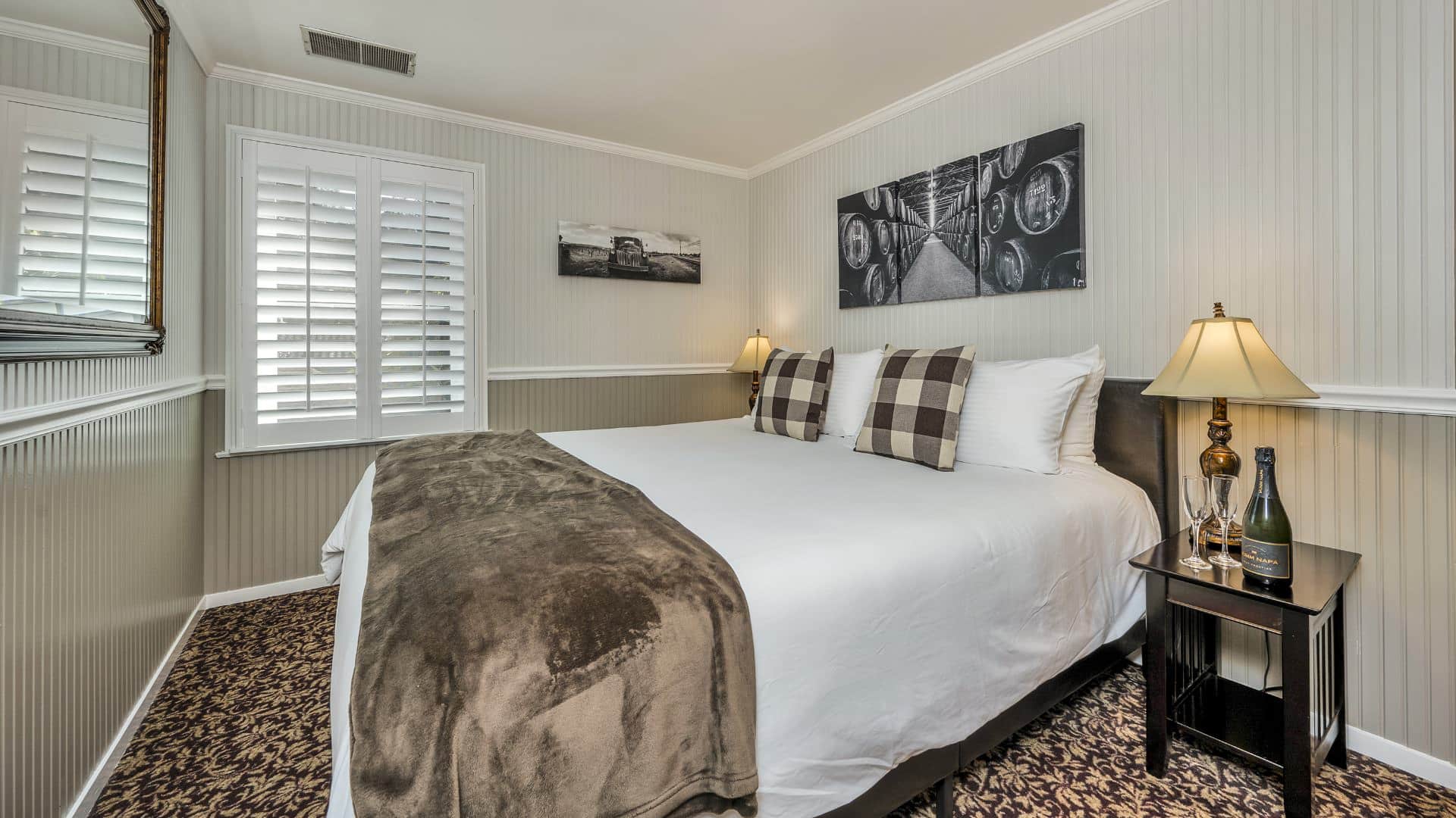 Bedroom with white walls, light gray wainscotting, floral carpeting, white bedding, and dark wooden nightstands