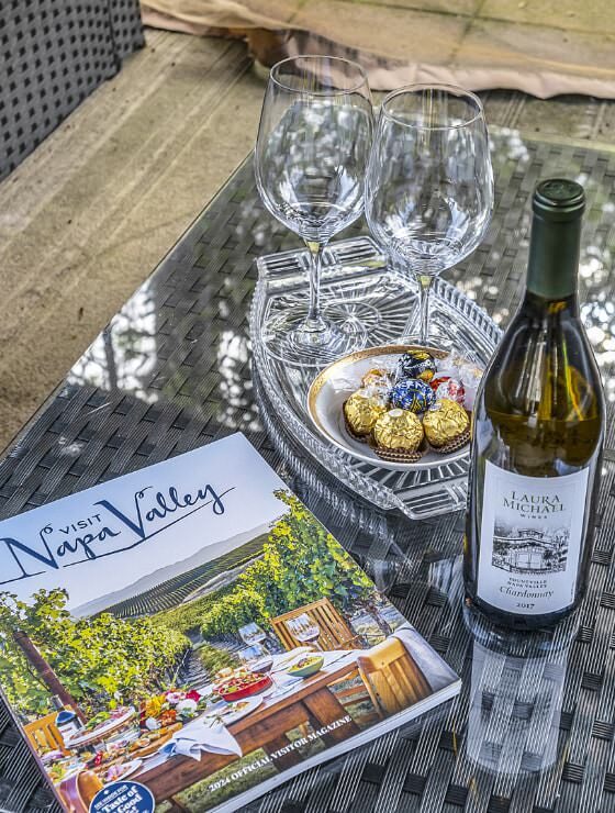 Visit Napa Valley book, bottle of white wine, and glass tray with wine glasses and chocolates on top of gray wicker patio coffee table