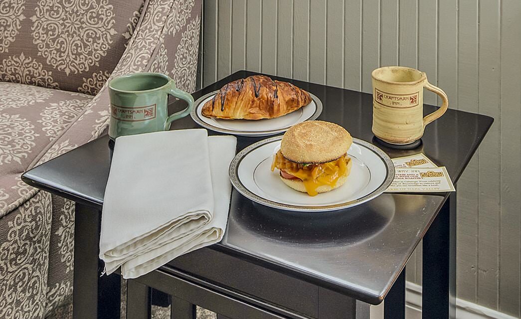 Brown side table with one white plate with a breakfast sandwich and another white plate with a chocolate croissant