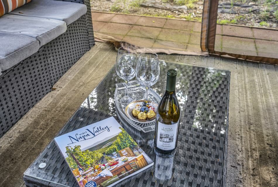 Visit Napa Valley book, bottle of white wine, and glass tray with wine glasses and chocolates on top of gray wicker patio coffee table