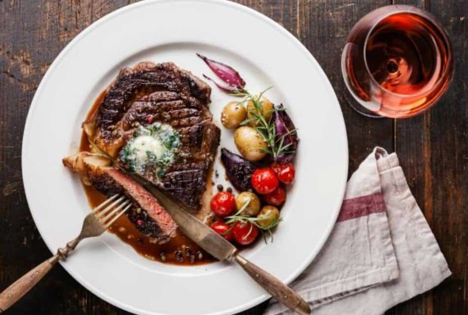Close up view of white plate with a partially cut steak and roasted tomatoes and potatoes
