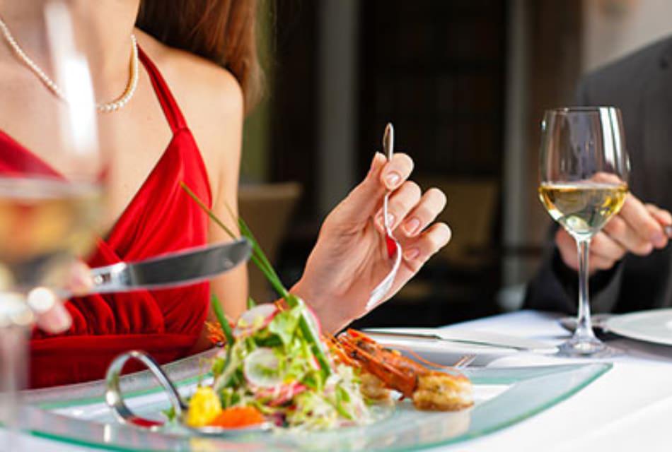 Lady in red dress holding a fork and knife about to eat a salad on a glass plate