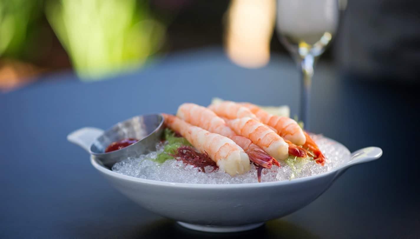 Shrimp over ice with ketchup condiment in white bowl on granite table outside with champagne in background; Napa Valley Wine Country