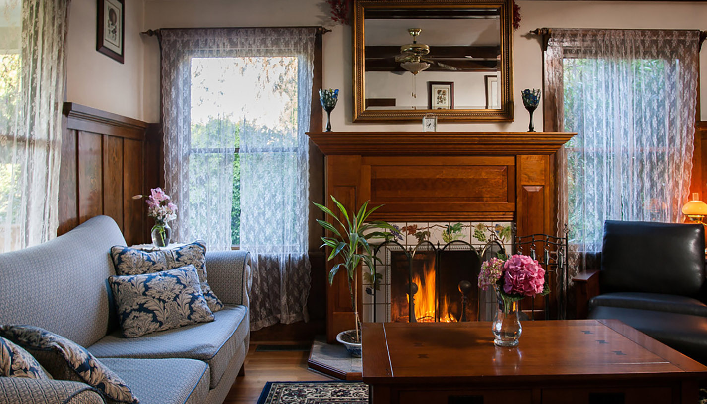 Living room of the Wine Way Inn with coach, armchair, coffee table, flowers, and fireplace in Calistpga, CA; Napa Valley, Wine Country