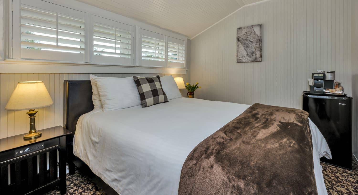 Bedroom with white walls, white trim, floral carpeting, white bedding, and black mini fridge
