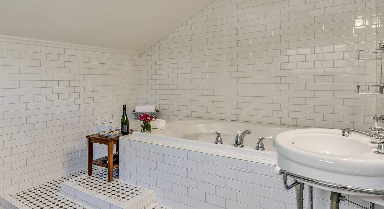 Bathroom with white tile on the walls and surrounding the tub and a white sink