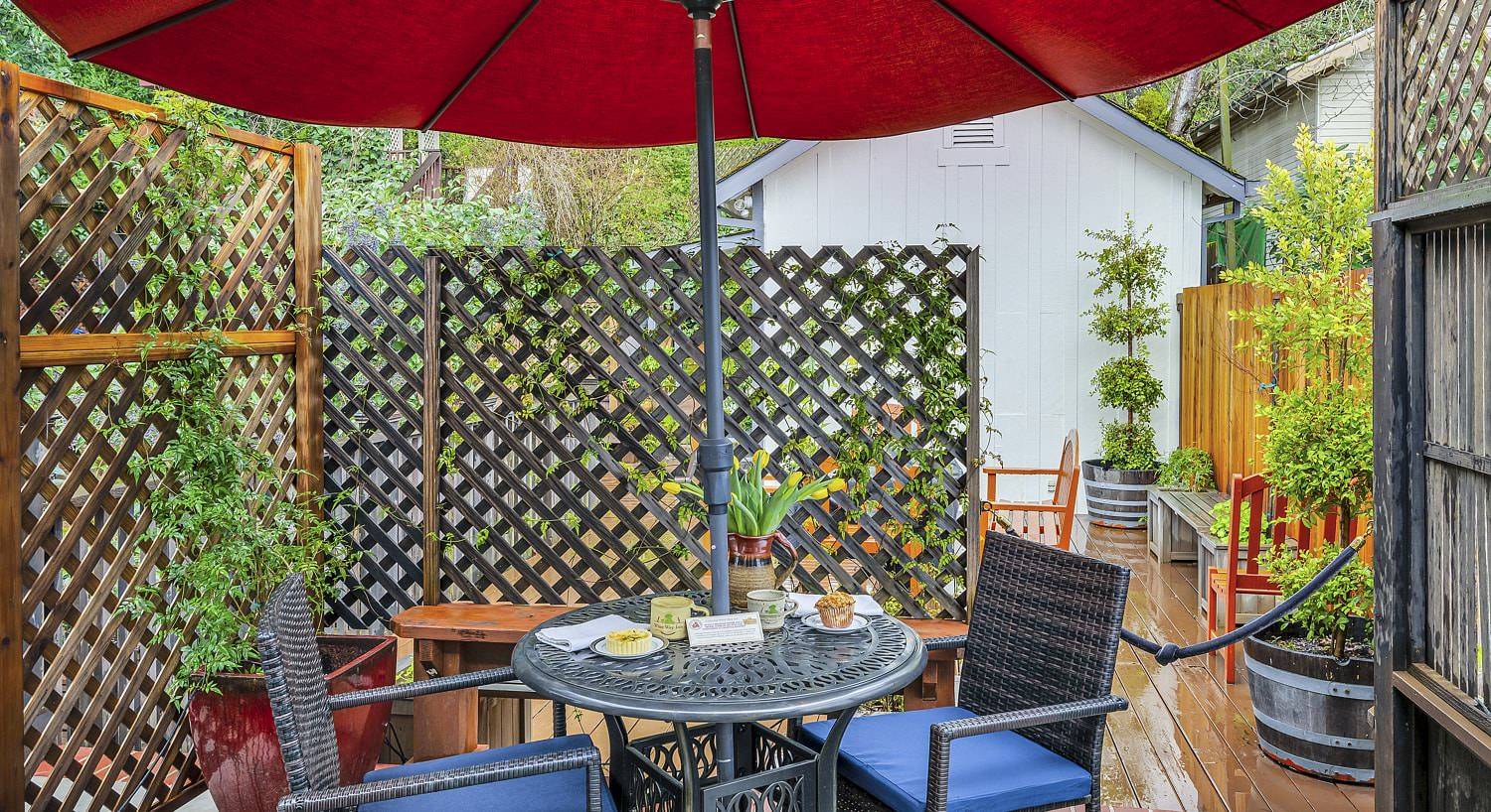 Metal patio table and wicker chairs on a wooden deck covered by a red umbrella