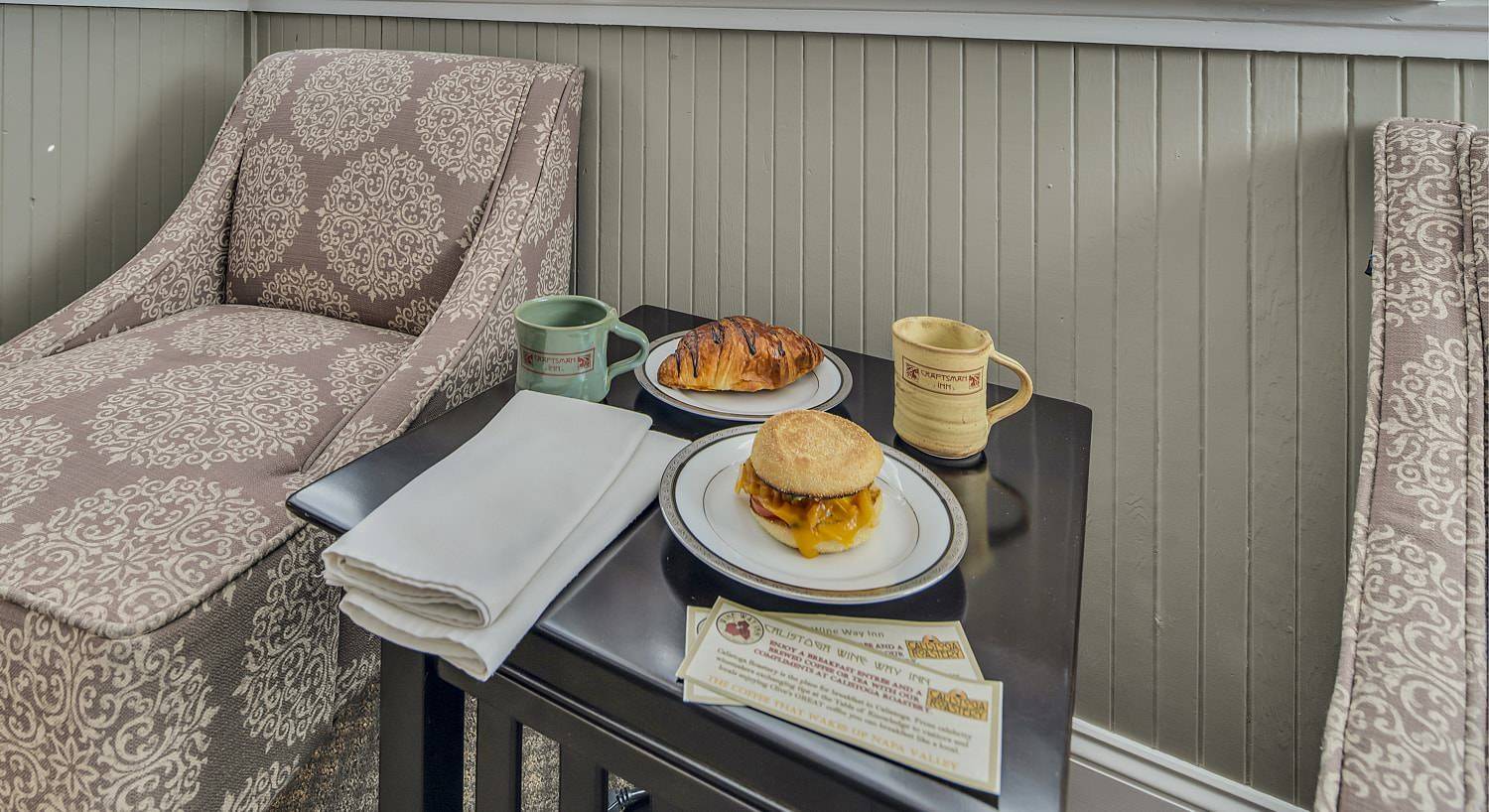 Brown side table with one white plate with a breakfast sandwich and another white plate with a chocolate croissant