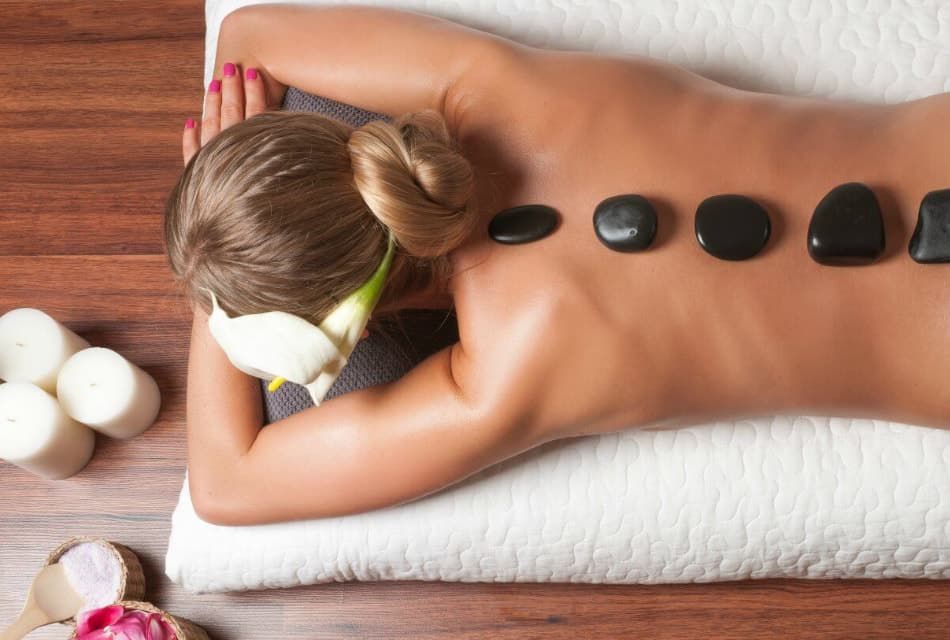 Woman laying on a white pillow face down with hot rocks in a line on her back