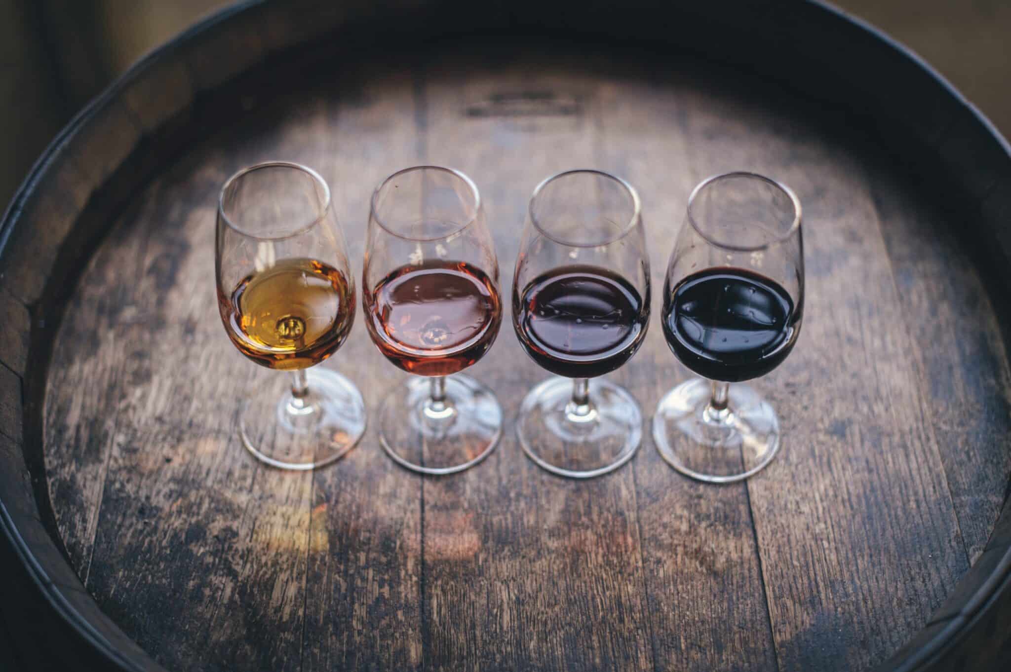Four wine glasses filled with different wines, sitting atop a wine barrel.