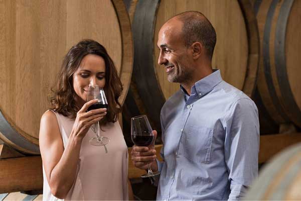 Romantic couple tasting a glass of red wine in a traditional cellar surrounded by wooden barrels.