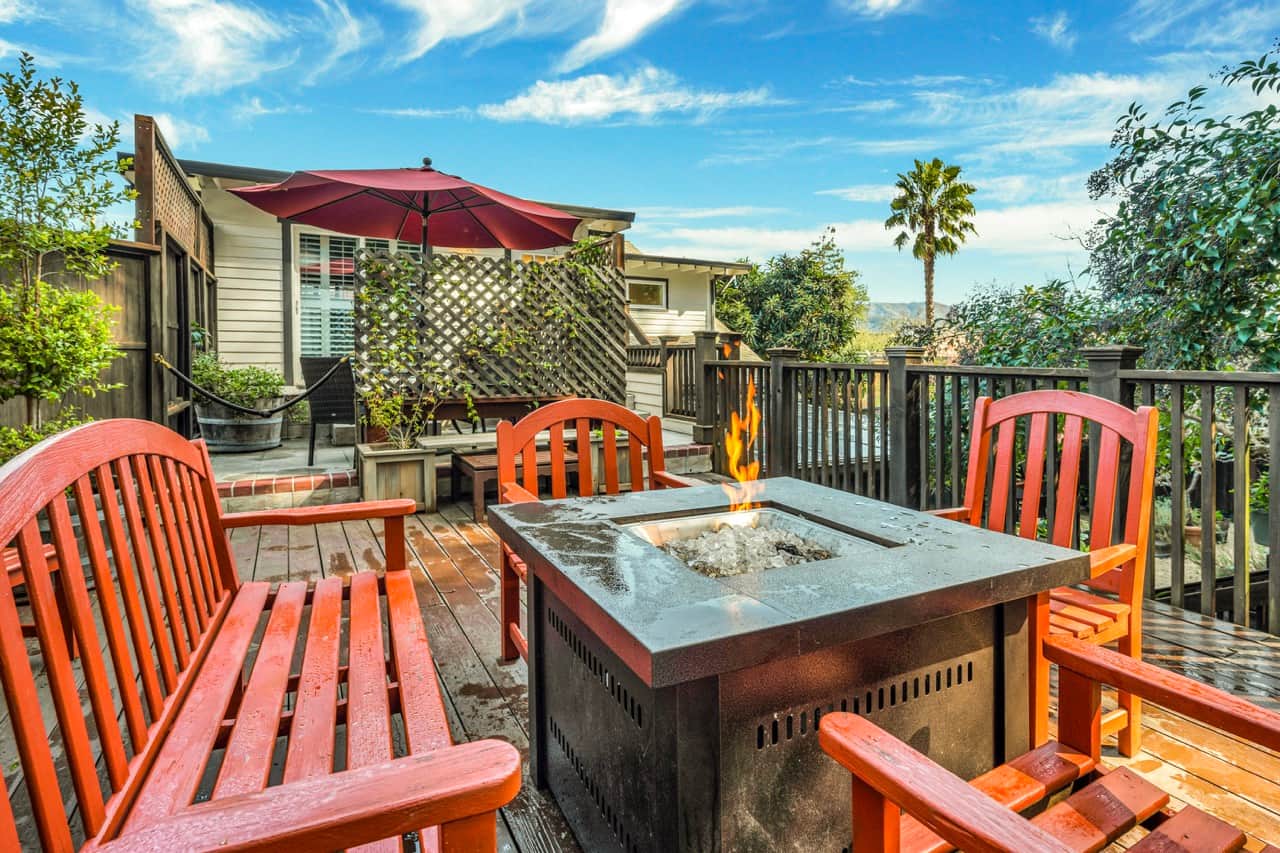 Orange wooden patio chairs and bench surrounding tabletop firepit on wooden deck