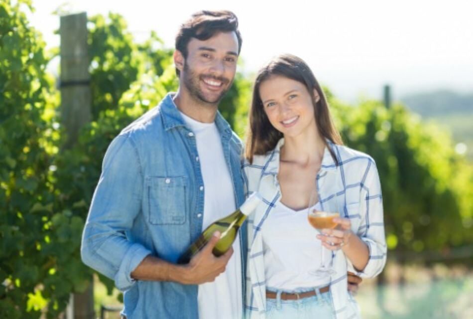 Man holding a bottle of wine and woman holding a class of wine with vineyard in the background